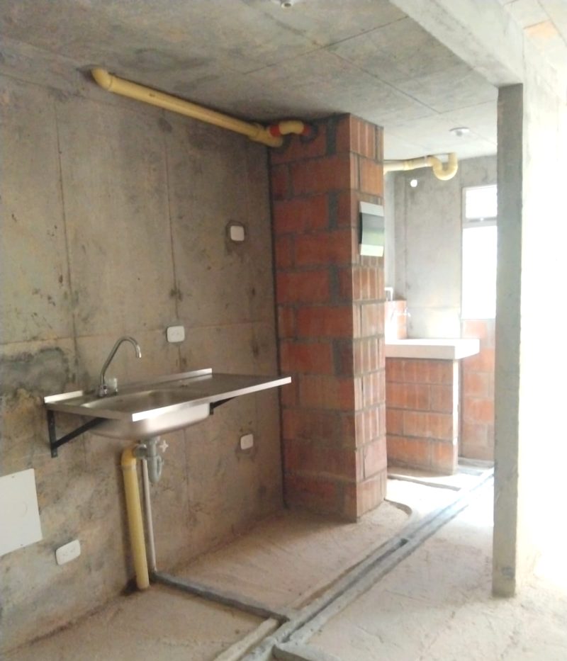 Cocina en obra gris, con ladrillo a la vista y tuberías sin terminar