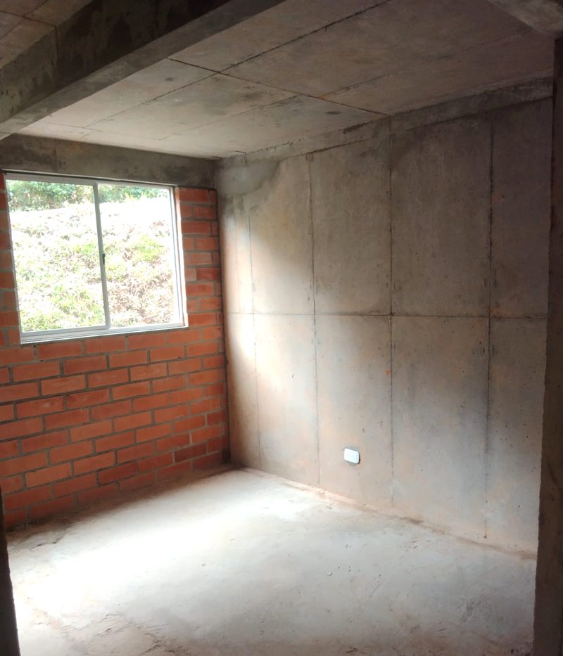 Sala en obra gris, con muro de ladrillo y piso de concreto