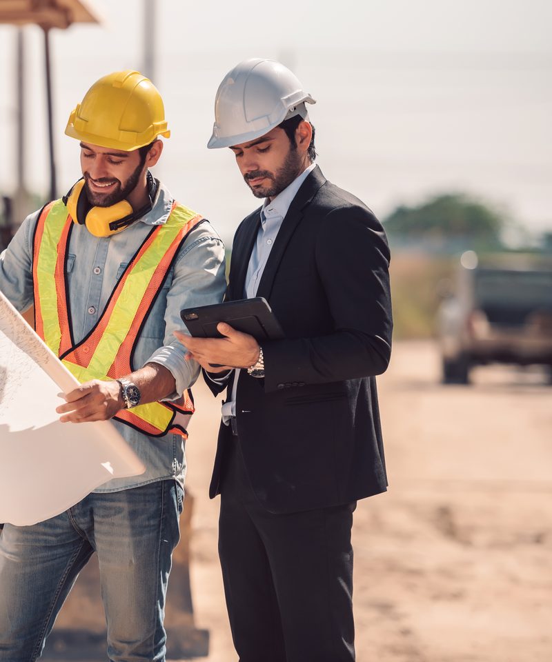 Maestro con el plano e ingeniero con la tablet, revisando una obra en construcción